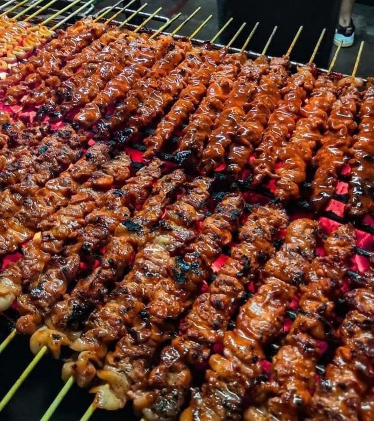 Suya skewers grilling over charcoal